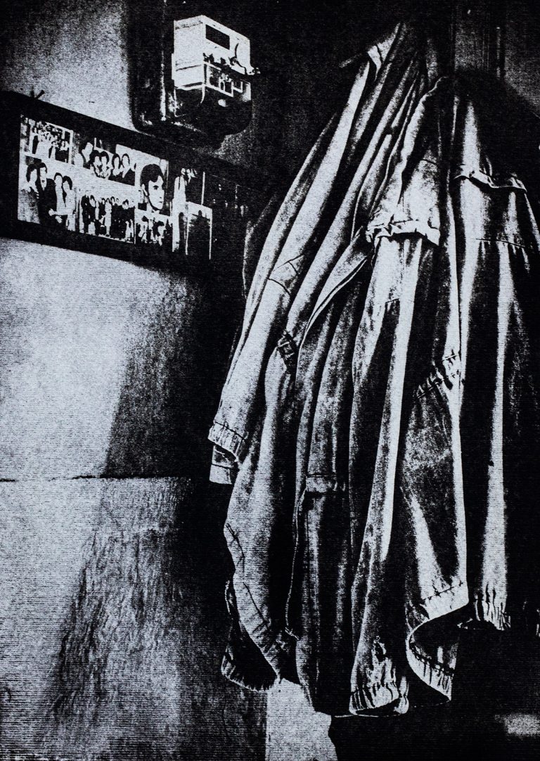 A monochromatic artwork titled 'Eastern Europe I' showing a hanging coat in a dimly lit room, with a photo collage of people on the wall to the left and a utility meter above them. The rough textures of the coat and wall create a worn, austere atmosphere, evoking themes of nostalgia and modest, working-class life. Unique handmade photographic artwork using the gumoil process by István Havadi-Nagy-David